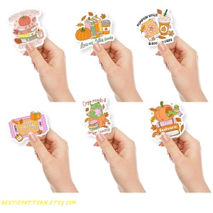 May include: A collection of fall-themed stickers featuring pumpkins, books, coffee, and autumn leaves. The stickers have text like "Cozy Readers," "Leaves, Lattes, Books," and "Pumpkin Spice & Book Vibes." The stickers are held in hands.