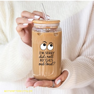 May include: A clear glass reusable tumbler with a bamboo lid and a straw. The tumbler is filled with iced coffee and has a sticker with two cartoon eyes and the text "I'm sorry did I roll my eyes out loud?"