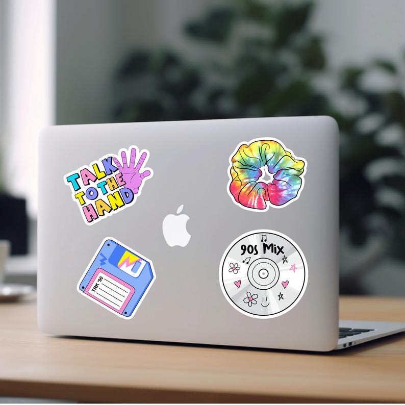May include: A laptop computer with five stickers on it. The stickers are a floppy disk, a scrunchie, a hand with the text "Talk to the Hand", a CD with the text "90s Mix", and a pink heart.