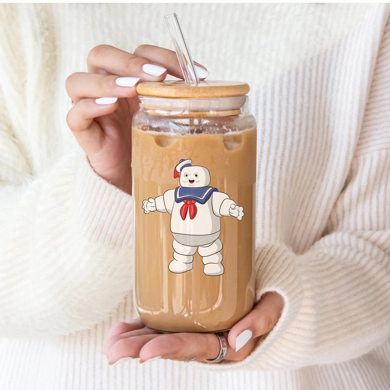 Puede incluir: Un tarro de vidrio transparente con tapa de bamb&uacute; y una pajita, lleno de una bebida marr&oacute;n. Un personaje de dibujos animados de un fantasma blanco con un gorro de marinero azul y una pajarita roja est&aacute; impreso en el tarro.