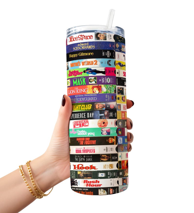 May include: A stainless steel tumbler with a colorful design featuring the titles of popular movies from the 1990s. The tumbler is wrapped with VHS tape covers, including "Office Space", "Edward Scissorhands", "Happy Gilmore", "The Lion King", "The Bodyguard", "Independence Day", "American Pie", "The Fugitive", "Hook", and "Rush Hour".