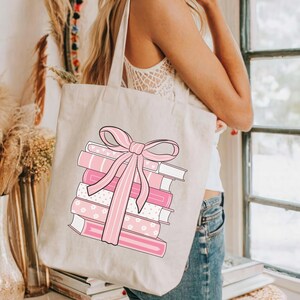 May include: Beige tote bag featuring a stack of pink books tied with a pink bow. The books have various patterns, including stripes and floral designs. The text "BESTIEPATTERN ETSY.COM" is printed at the bottom of the bag.