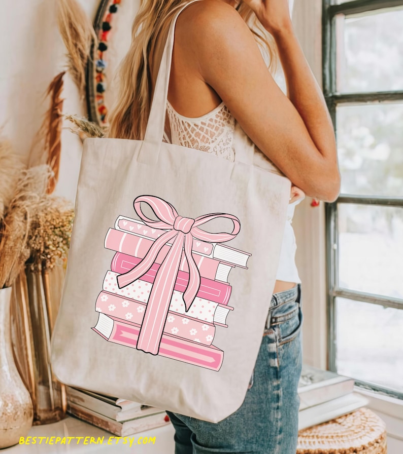 May include: Beige tote bag featuring a stack of pink books tied with a pink bow. The books have various patterns, including stripes and floral designs. The text "BESTIEPATTERN ETSY.COM" is printed at the bottom of the bag.