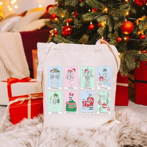 May include: A white canvas tote bag with a colorful design of skeletons celebrating Christmas. The bag features the text "The Misletoe", "The Office", "The Reindeer", "The Christmas Sweater", "The Christmas Movie Marathon", and "The Ornaments".