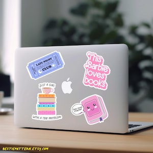 May include: A laptop covered in stickers with a reading theme. Stickers include a blue ticket, a pink book with a face, and text that reads "This Barbie loves books" and "Just a girl with a TBR problem."
