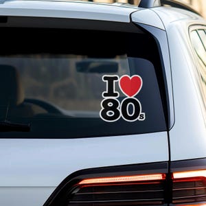May include: A white car with a black and red sticker that says "I love 80s" on the rear window.