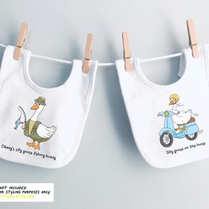 May include: Two white bibs with different designs. One bib features a cartoon goose wearing a fishing hat and holding a fishing rod. The text on the bib reads "Daddy's silly goose fishing buddy". The other bib features a cartoon goose riding a blue scooter. The text on the bib reads "Silly goose on the loose".