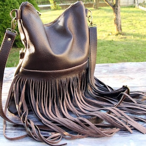 May include: A brown leather handbag with a fringe detail. The bag has a long strap and a top zipper closure.