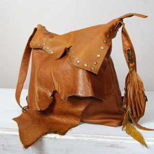 Peut inclure: Sac à dos en cuir marron fait à la main, avec un design texturé unique. Le sac est doté d'un rabat orné de clous en laiton et d'un pompon décoratif avec des plumes. Il possède des bretelles réglables et un intérieur spacieux.