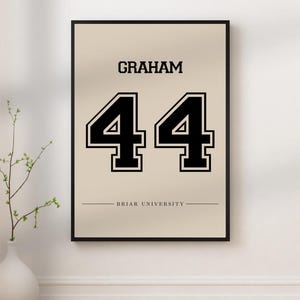 Może przedstawiać: Oprawiona grafika ścienna z napisem "Graham" nad numerem "44" w kolorze czarnym, z czarną obwódką. Tekst "Briar University" znajduje się pod numerem. Tło jest w kolorze jasnobeżowym.