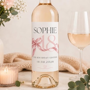 May include: A clear glass wine bottle featuring a white label with the name SOPHIE in black text, a large pink number 18, a pink ribbon graphic, and the text THE BIRTHDAY EDITION 18.08.2026 with a small heart icon at the bottom of the label.