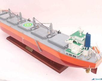 Può includere: Un modello dettagliato di una grande nave da carico arancione e grigia con una sovrastruttura verde e bianca. La nave è montata su una base in legno ed è un modello in scala.