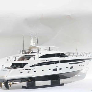 Puede incluir: Un yate modelo blanco y negro con el texto "IMPERIAL PRINCESS" en el lateral. El yate tiene un diseño elegante con múltiples cubiertas, ventanas y barandillas. Se encuentra sobre un soporte negro.