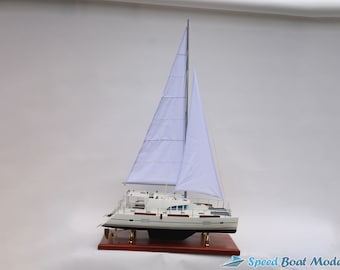 May include: A scale model of a white catamaran sailboat featuring two tall white fabric sails, a detailed deck structure, and a dark hull. The model is mounted on a rectangular wooden base and includes the text Speed Boat Model in the corner.