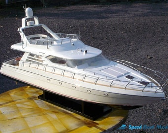 Può includere: Modello di yacht bianco con un'antenna radar sulla cima, uno scafo bianco e una base nera. Lo yacht è su una superficie gialla e marrone.