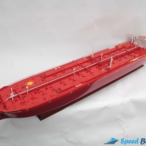 Pode incluir: Um modelo de navio vermelho de um grande petroleiro com um convés branco e marcas amarelas. O navio está sobre uma base de madeira.