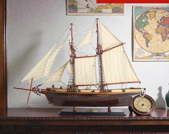 May include: A detailed wooden model sailboat, labeled "HARVEY", with cream-colored sails and intricate rigging. The model is displayed on a dark wooden surface. The dimensions are 23.6 inches long, 7.1 inches wide, and 26.8 inches high.