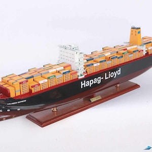 May include: A detailed model of a container ship, the "Colombo Express", painted in red, black, and white with yellow containers. The ship is labeled "Hapag-Lloyd" and is displayed on a wooden base.