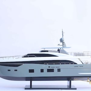 Puede incluir: Maqueta de yate en tonos grises, negros y blancos, montada sobre un soporte negro. El yate presenta múltiples cubiertas, ventanas y una antena de radar. El casco es gris, con una franja negra a lo largo de las ventanas.