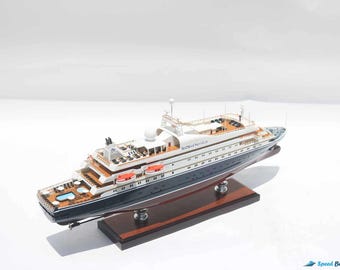 May include: A detailed model of a luxury yacht, featuring a dark blue hull and white superstructure. The model includes intricate details like deck furniture, lifeboats, and a small pool. It rests on a wooden base, showcasing the yacht's design.