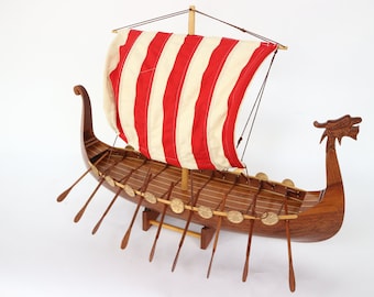 May include: A wooden model of a Viking ship with a red and white striped sail. The ship has a dragon head at the bow and oars on the sides.