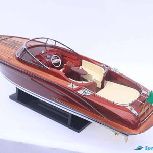 May include: A mahogany and white speedboat model with a wood deck and an Italian flag. The model is on a black display stand.