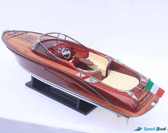 May include: A mahogany and white speedboat model with a wood deck and an Italian flag. The model is on a black display stand.