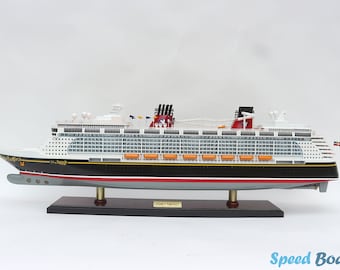 Può includere: Un modello dettagliato della nave da crociera Disney Dream, con uno scafo bianco con accenti rossi e neri. La nave ha più ponti con scialuppe di salvataggio e un logo di Topolino sulla prua. Il modello è esposto su una base di legno con l'iscrizione "Disney Dream".