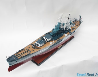 May include: A detailed model of a battleship with a wooden deck, gray and white hull, and black guns. The model is displayed on a wooden base.