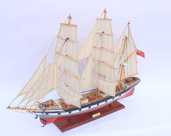 May include: A detailed scale model of the tall ship Glenlee, featuring three masts with cream-colored sails, a black and white hull with a red lower section, and a red flag at the stern. The ship is mounted on a polished wooden display base.