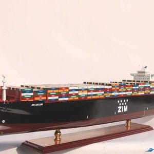 May include: A detailed model of a ZIM container ship, the ZIM CHICAGO, with a black hull and a red bow. The ship is loaded with colorful shipping containers and is displayed on a wooden base.