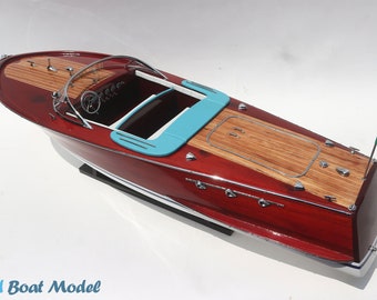 Può includere: Un modello di motoscafo in legno rosso con interni blu e bandiera italiana bianca e verde. Il modello è su un supporto in legno.