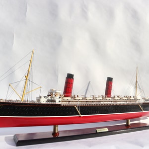 Könnte beinhalten: Ein detailliertes Modell der RMS Carpathia, ein britisches Ozeandampfschiff, mit rotem und schwarzem Rumpf, gelben Masten und vier roten Schornsteinen. Das Modell wird auf einem Holzsockel präsentiert.