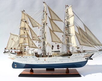 Può includere: Modello dettagliato di veliero con vele bianche e scafo blu. La nave ha più alberi e sartiame, con accenti rossi. Poggia su una base di legno, mostrando l'artigianato e il design nautico.