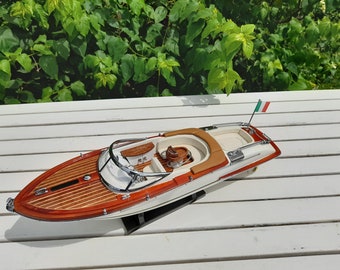 Può includere: Un modello in legno di un motoscafo bianco e marrone con interni beige. La barca ha una piccola bandiera italiana sul retro.