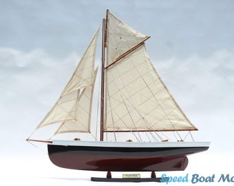May include: A model sailboat with cream-colored sails and a dark brown hull. The boat has a black and white trim along the top edge. The word "PURITAN" is visible on a small plaque at the base of the model.