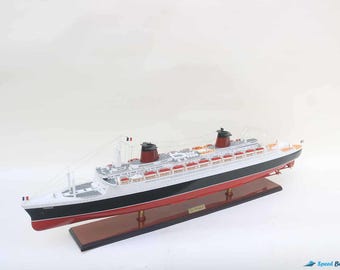 Può includere: Un modello dettagliato della nave da crociera Queen Mary 2, esposto su una base di legno. La nave presenta uno scafo bianco con una striscia nera, dettagli rossi e due fumaioli rossi e neri. Il modello include dettagli intricati.