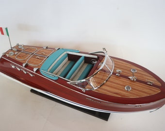 Può includere: Un modello di barca in legno rosso con interni color turchese e una bandiera italiana bianca e verde a prua.