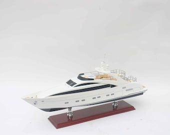 May include: A scale model of a white luxury yacht with dark blue window accents and a tan deck. The vessel features a multi-level structure with railings and is mounted on two silver supports attached to a rectangular dark wood display base.