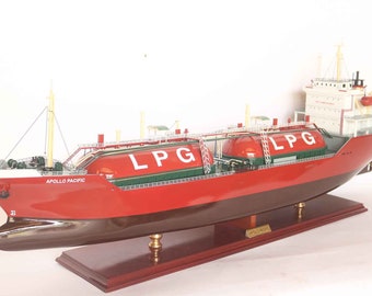 Può includere: Un modello di nave rosso e bianco con il nome "APOLLO PACIFIC" sul lato. La nave ha diversi grandi serbatoi cilindrici etichettati "LPG" sul ponte. La nave è su una base di legno.