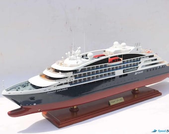 May include: A detailed model of the PONANT EXPLORER cruise ship. The model features a dark blue hull with a red waterline, white superstructure, and multiple decks. The model sits on a wooden base with a nameplate.