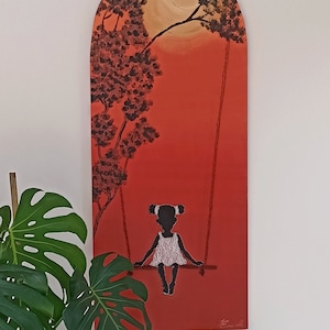 Könnte beinhalten: Ein bogenförmiges Leinwandgemälde zeigt die Silhouette eines Mädchens auf einer Schaukel vor rotem Hintergrund. Das Kunstwerk zeigt einen Baum mit dunklen Blättern und eine helle Sonne. Das Gemälde hängt an einer weißen Wand, mit grünen Pflanzen im Vordergrund.