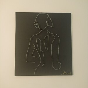 Könnte beinhalten: Schwarze Leinwandkunst mit einer minimalistischen Strichzeichnung einer Person von hinten. Die Figur ist mit silbernem Faden umrandet, die Signatur des Künstlers befindet sich unten rechts. Das Kunstwerk ist auf einer quadratischen Leinwand montiert.