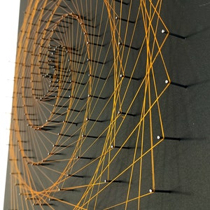 Könnte beinhalten: Orangefarbene String Art auf schwarzem Hintergrund. Die Schnur ist in einem Spiralmuster zwischen Nägeln gespannt.