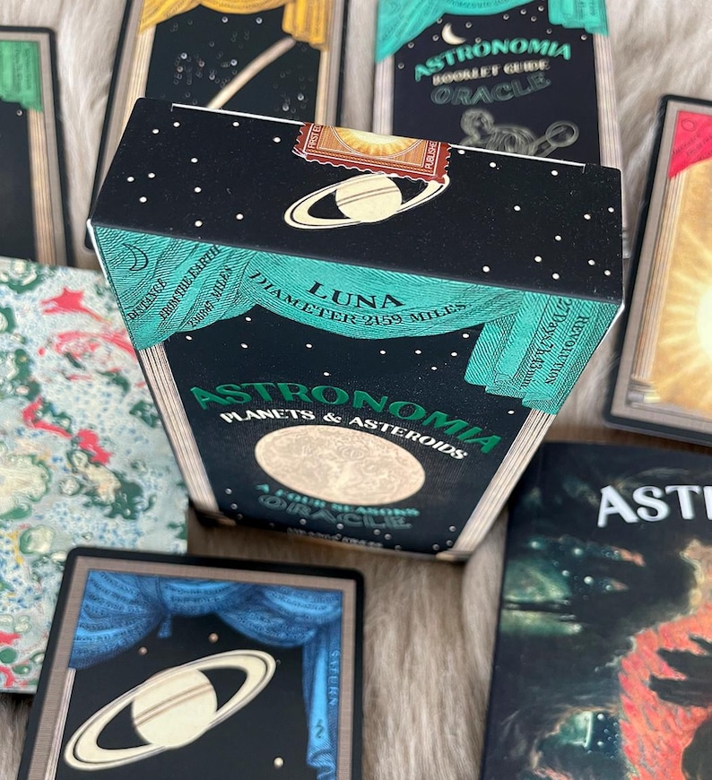 May include: A black box with gold and green accents featuring the text "Astronomia Planets & Asteroids" and "Luna Diameter 2159 Miles". The box is decorated with a celestial scene and stars.