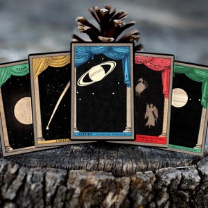 May include: Five vintage playing cards with celestial imagery. Each card features a different celestial body, including the moon, a comet, Saturn, a constellation, and a star. The cards are decorated with ornate frames and have a dark background.