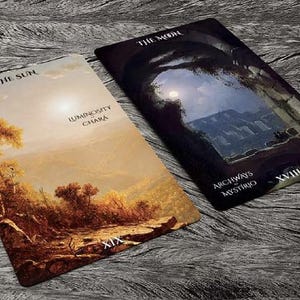May include: Two tarot cards, "The Sun" and "The Moon", from the "Archways of Mystery" deck. The Sun card depicts a landscape with a large tree and a bright sky. The Moon card shows a dark, moonlit scene with an archway and a distant mountain range.