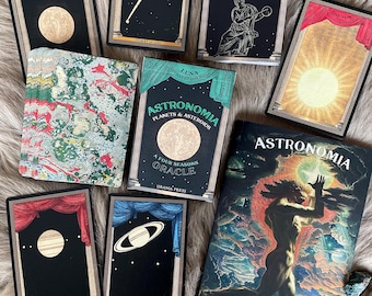 Peut inclure: Un jeu de cartes d'oracle avec un guide d'accompagnement. Les cartes présentent des illustrations de corps célestes, tels que la lune, les planètes et les étoiles. Le guide a une illustration en noir et blanc d'une personne debout dans un ciel nuageux. Les cartes et le guide font partie du jeu d'oracle Astronomia.