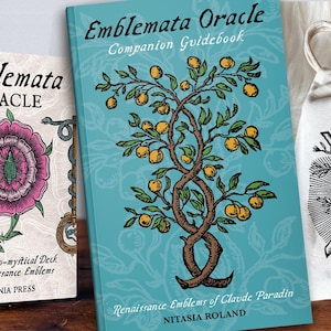May include: The Emblemata Oracle deck set includes a white box with a pink flower and key illustration, a teal companion guidebook featuring a tree with yellow fruit, and a white drawstring pouch with a black and white branch graphic.