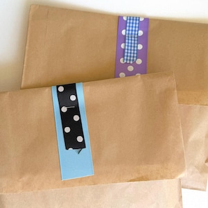 May include: Three brown paper packages are sealed with decorative ribbons. One ribbon is black with white polka dots and a light blue border. Another is purple with white polka dots and a blue and white gingham pattern. The third package is partially visible.